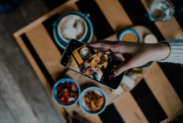 Hand holding smartphone photographing Instagrammable food and drinks.