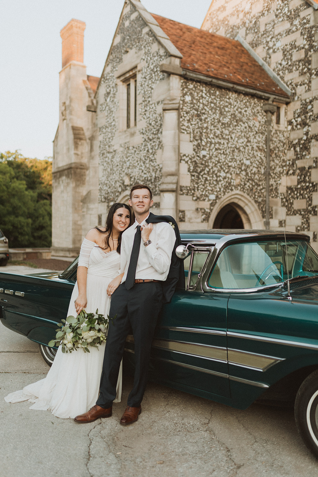 Chloe Schumacher and her husband at their wedding, posing with a classic car.