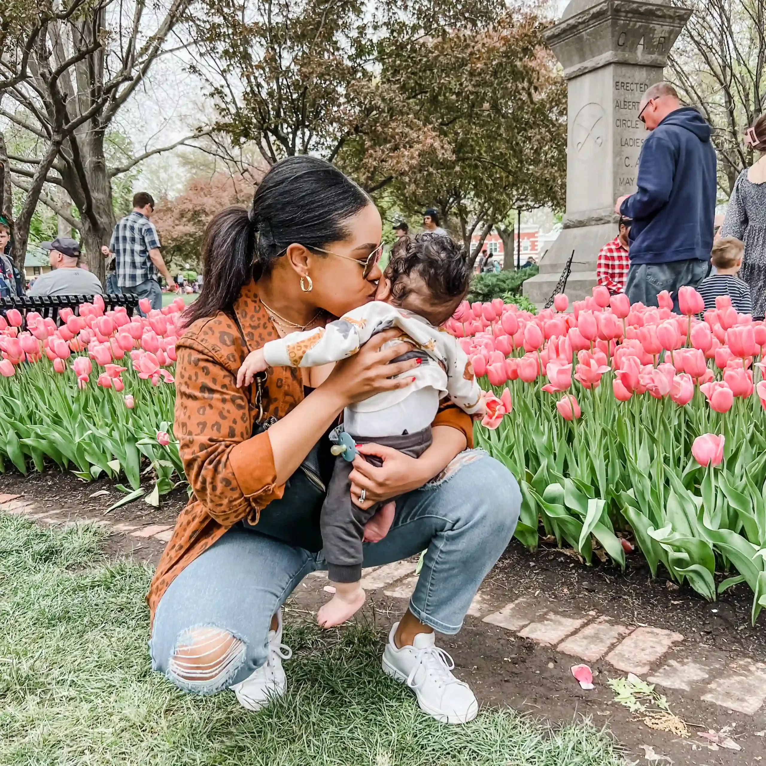 Ashlhea Demianovich with baby surrounded by pink tulips, reflecting her colorful personality and passions.