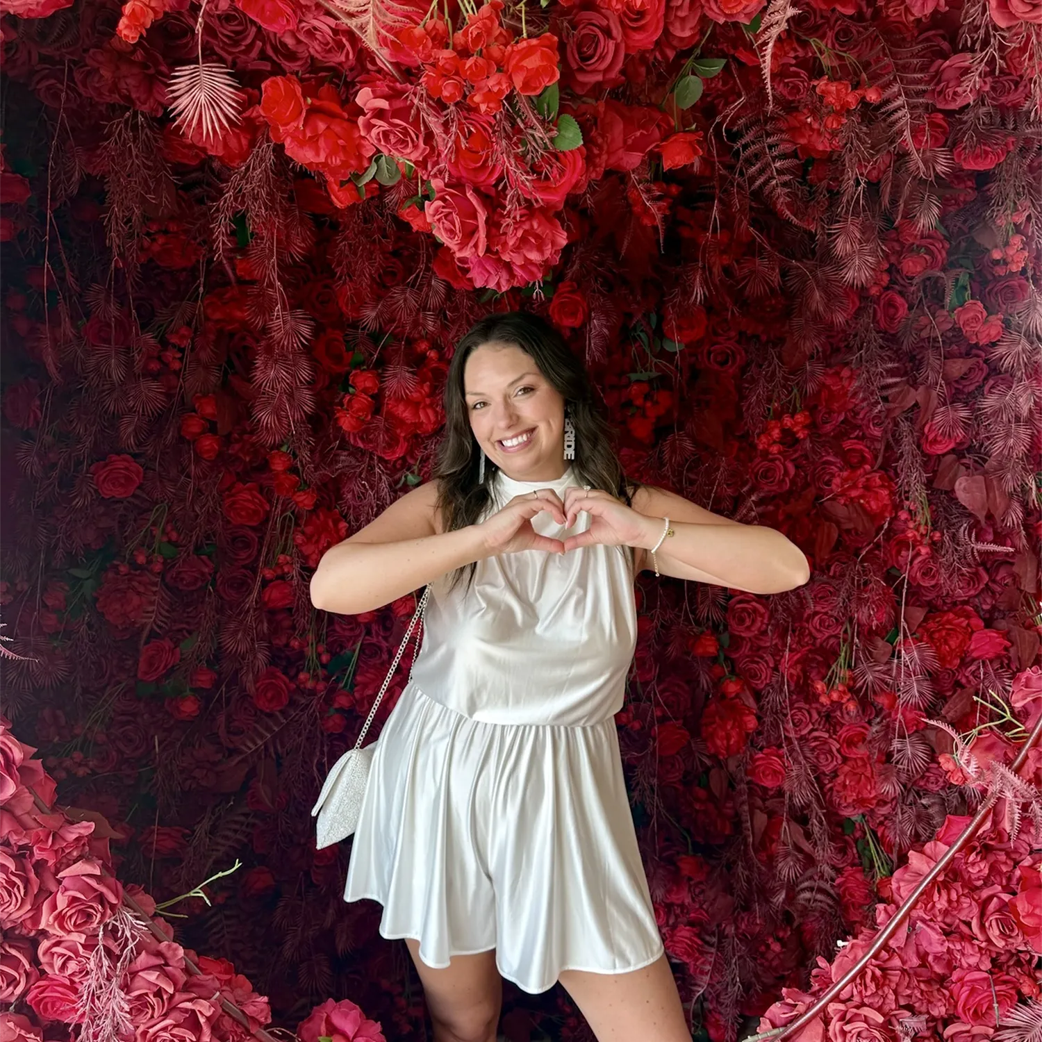 Jordan Johnson smiling and making heart shape with her hands in front of a vibrant red floral backdrop.