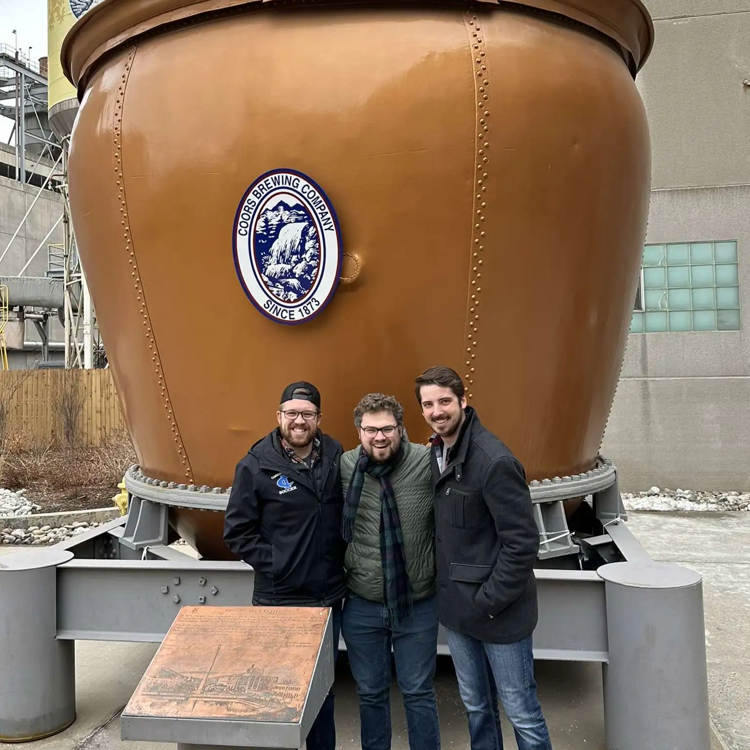Cameron Blom and colleagues posing with Coors Brewing Company tank, illustrating professional background and expertise.